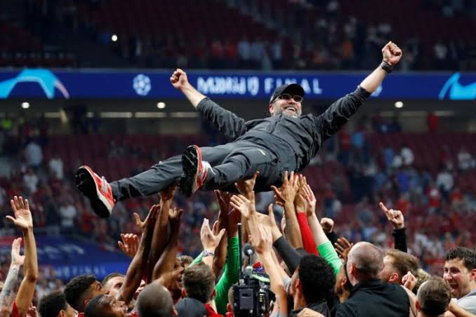 Jurgen Klopp being celebrated by Liverpool players and backroom staff after winning the Champions League.
